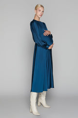 Woman wearing a long blue dress with white boots on a gray background