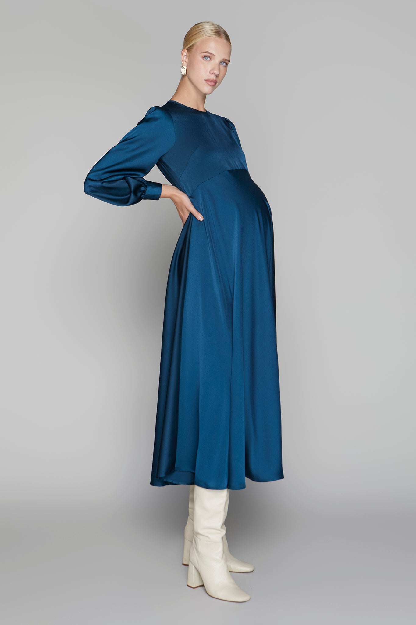 Woman wearing a blue dress with long sleeves and white boots on a gray background