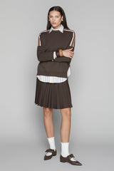 Woman wearing a brown sweater and pleated skirt with white shoes on a gray background