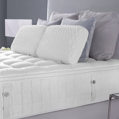 White mattress with decorative pillows on a bed against a gray wall.