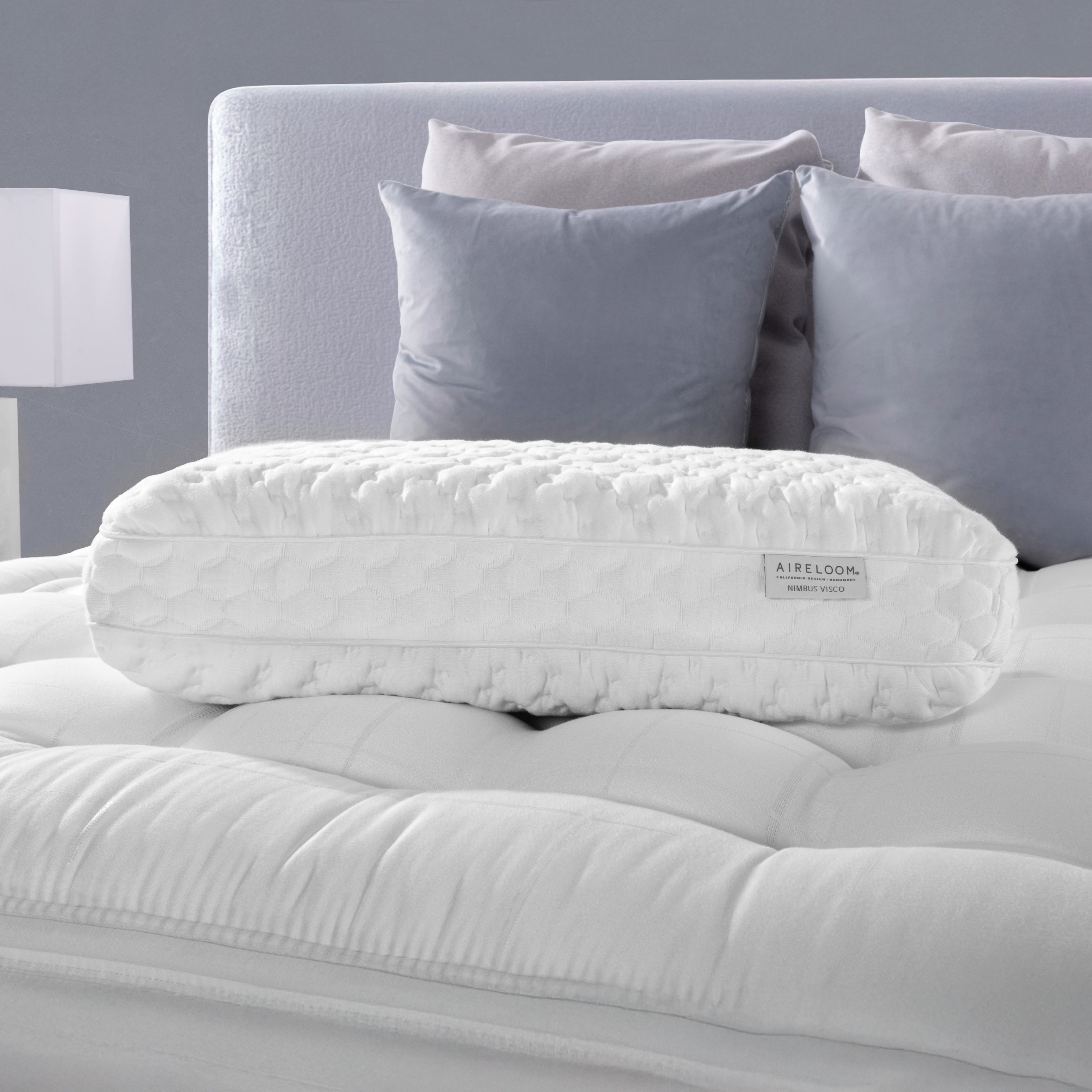 White contour pillow on a bed with gray headboard and pillows
