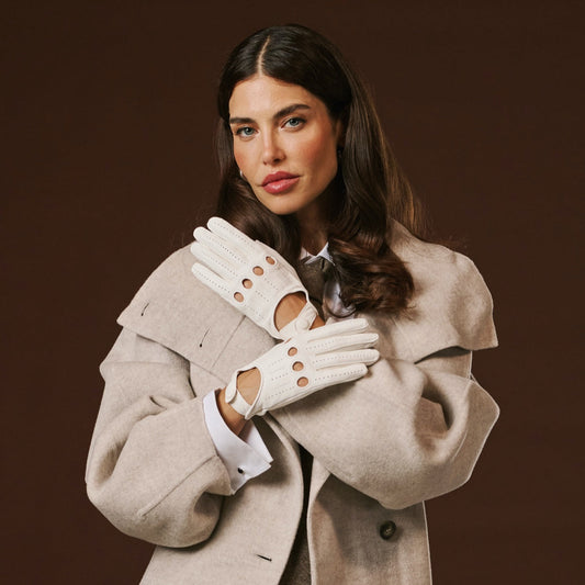 Woman wearing a beige coat and white gloves against a brown background
