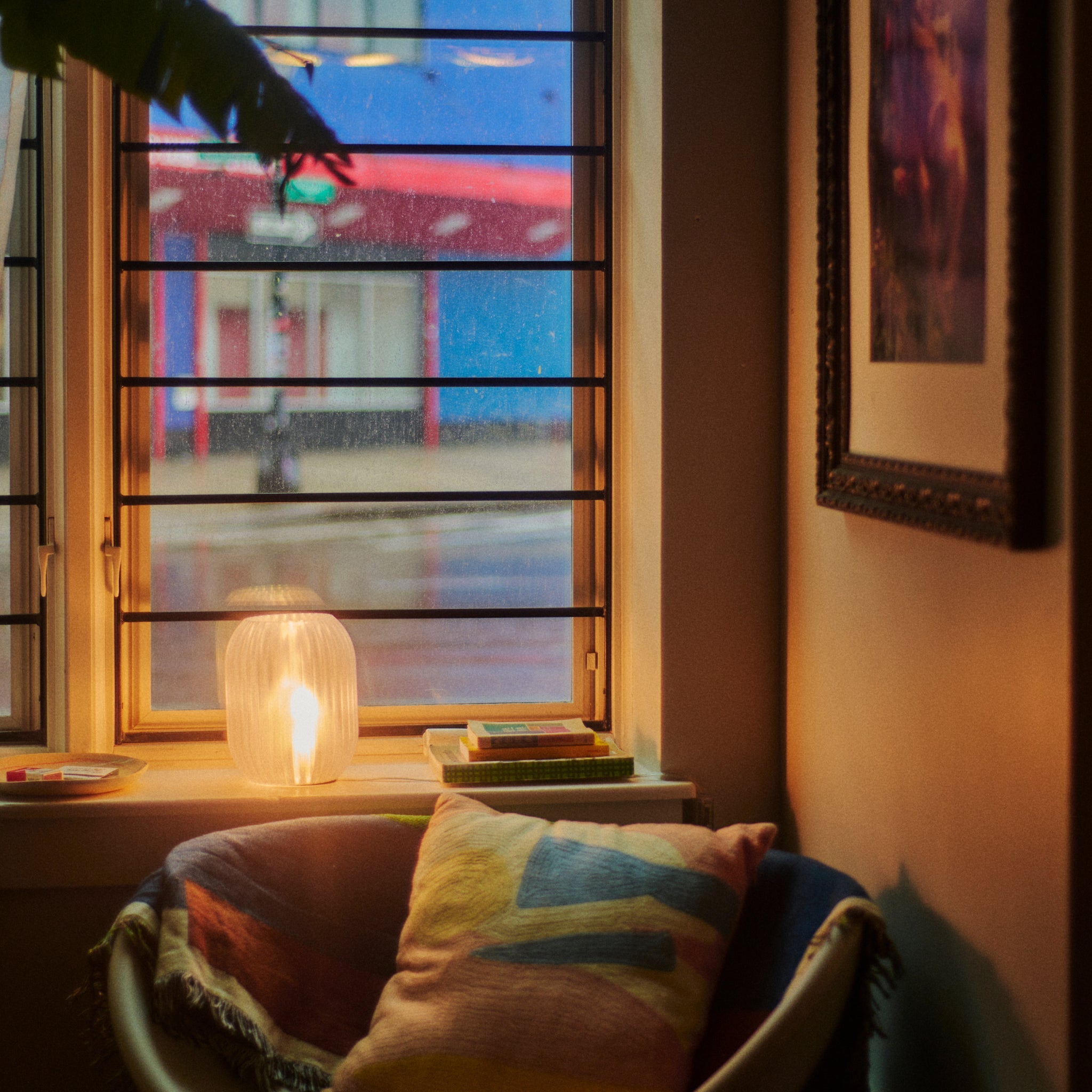 Cozy room with a window, candle, and colorful pillow.