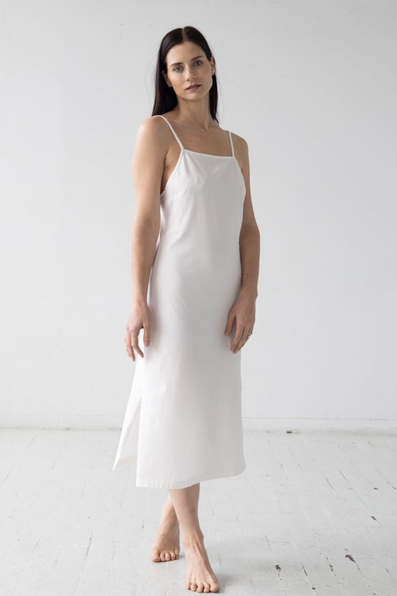Woman wearing a white slip dress against a plain background