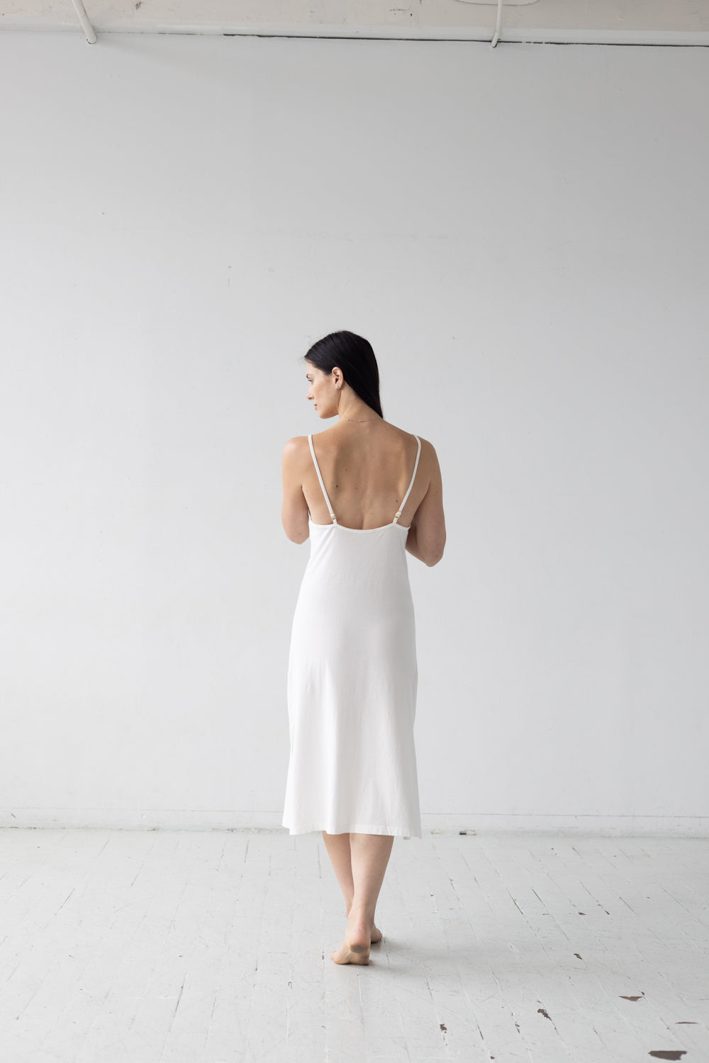 Woman wearing a white dress standing against a plain white wall.