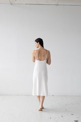 Woman wearing a white dress standing against a plain white wall.