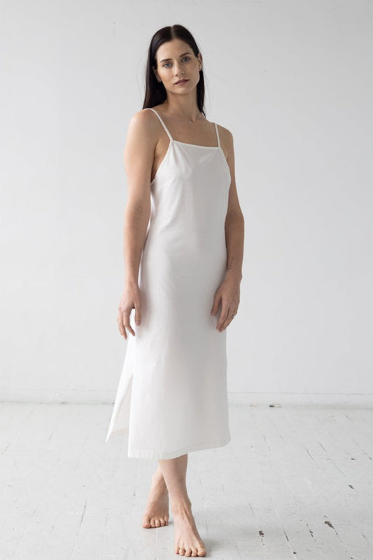 Woman wearing a white slip dress against a plain background