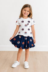 Young girl wearing a white t-shirt with red and blue graphics and a navy skirt with matching graphics on a light background.