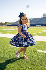 Young girl in a blue checkered dress with a bow standing on a football field.
