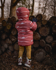 Child in a red coat standing next to a stack of logs in a forest