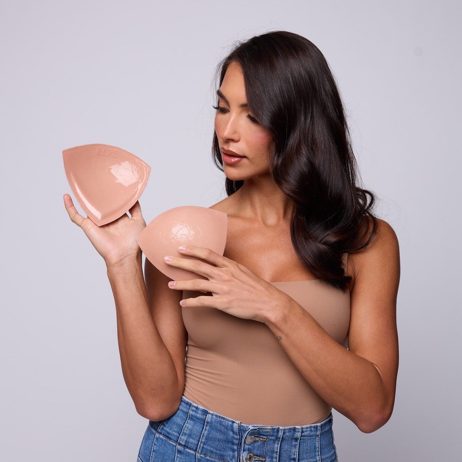Woman holding two silicone breast forms against a plain background