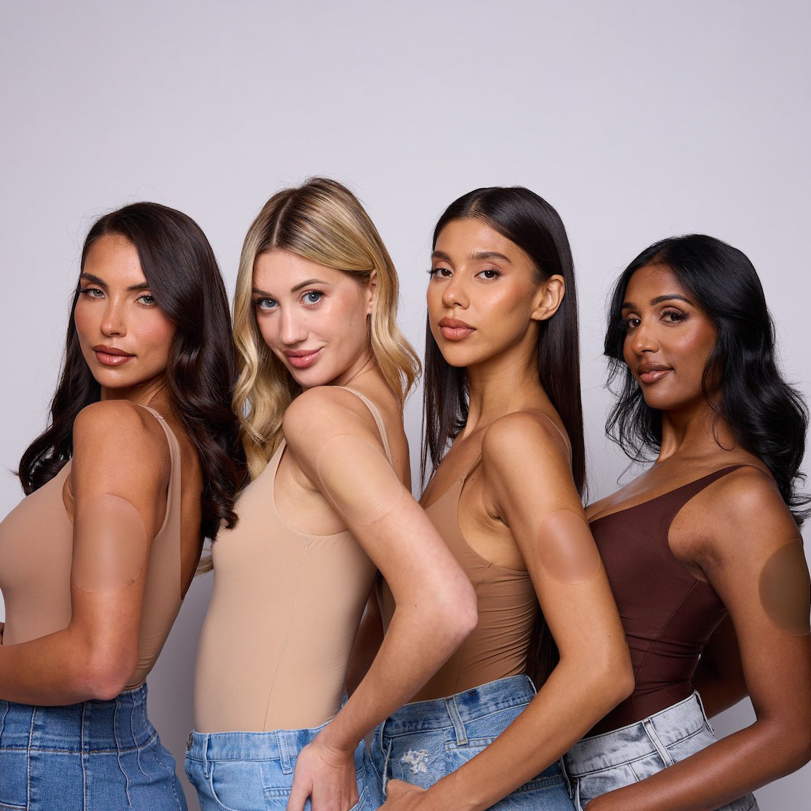 Four women wearing tank tops and jeans against a plain background