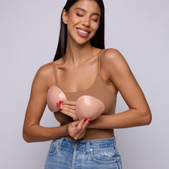 Woman holding pink breast forms against a plain background