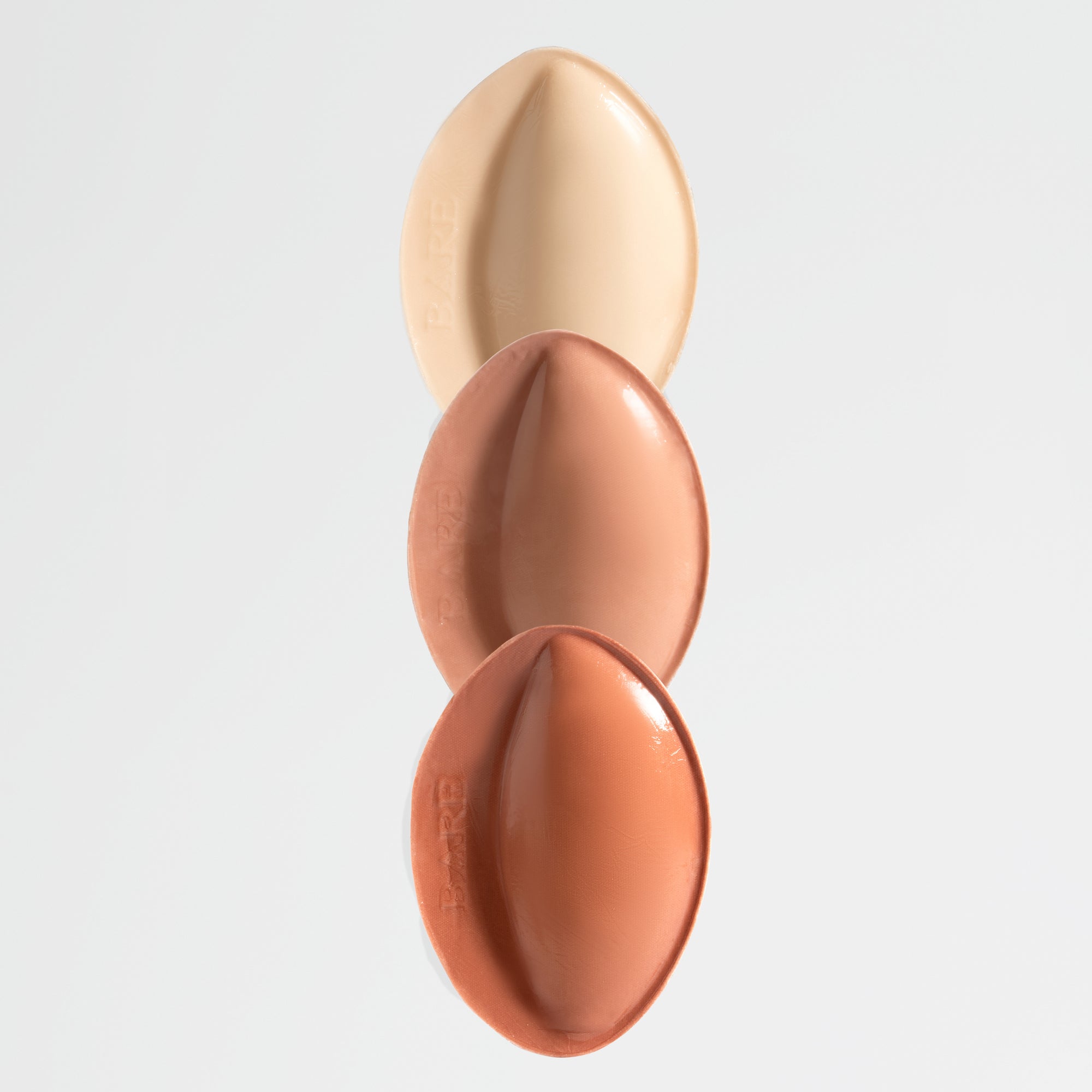 Three oval-shaped makeup products in beige, brown, and terracotta on a light gray background