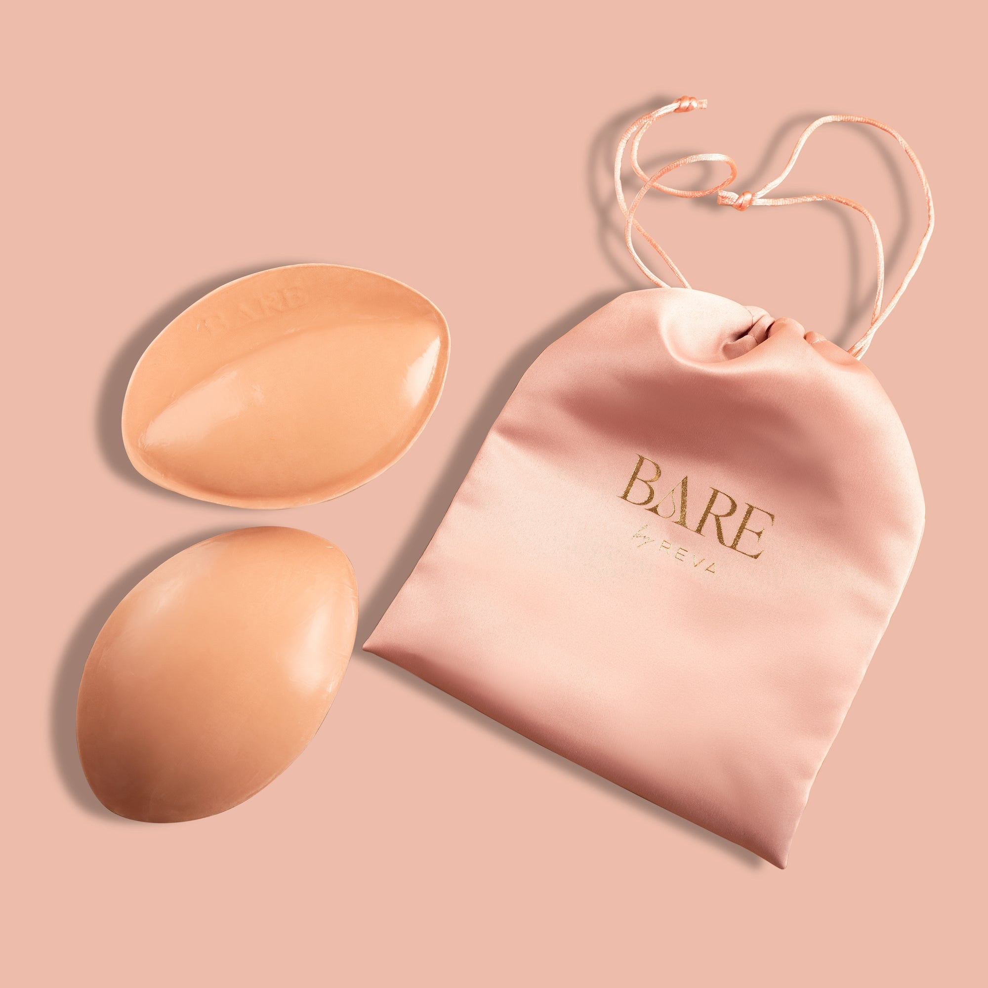 Two silicone bra pads and a pink pouch with 'BARE' branding on a pink background.