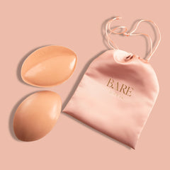 Two silicone bra pads and a pink pouch with 'BARE' branding on a pink background.