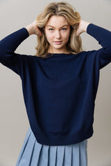 Woman wearing a navy blue sweater and light blue skirt against a plain background