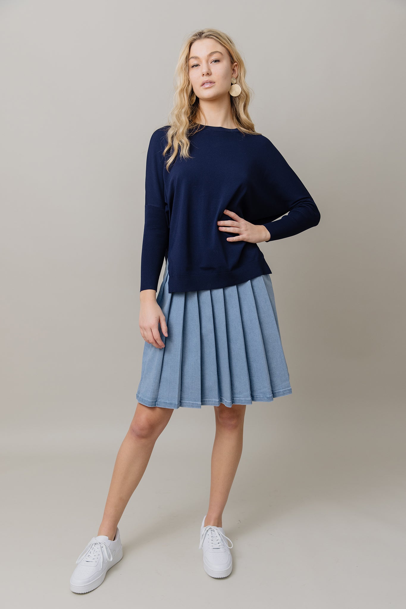 Woman wearing a navy sweater and light blue pleated skirt on a beige background