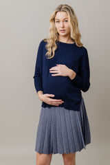 Pregnant woman wearing a navy sweater and gray pleated skirt against a plain background