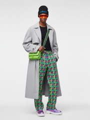 Person wearing a gray coat, colorful pants, and a green bag on a white background