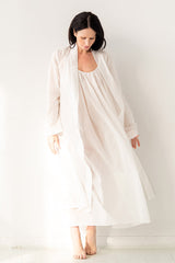 Woman wearing a long white nightgown with a matching robe against a plain background