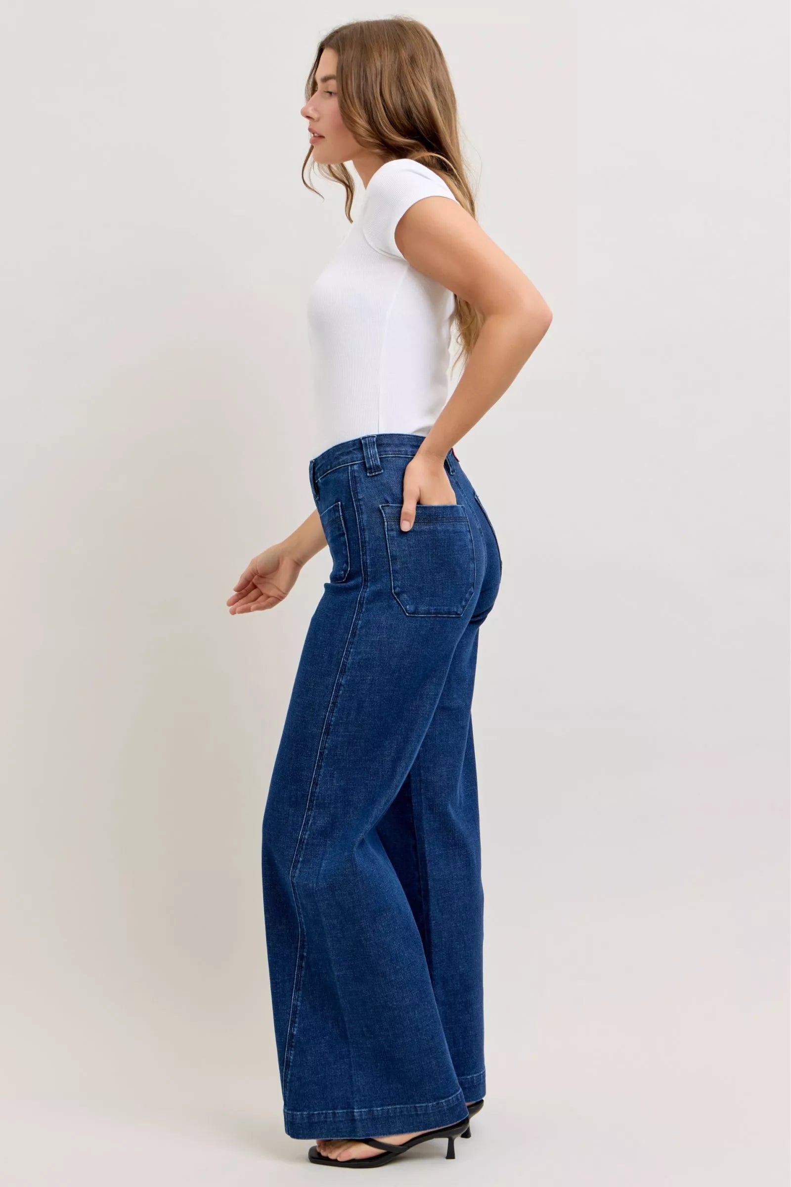 Woman wearing blue wide-leg jeans and a white top on a plain background