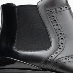 Close-up of a black leather shoe with detailed stitching on a white background