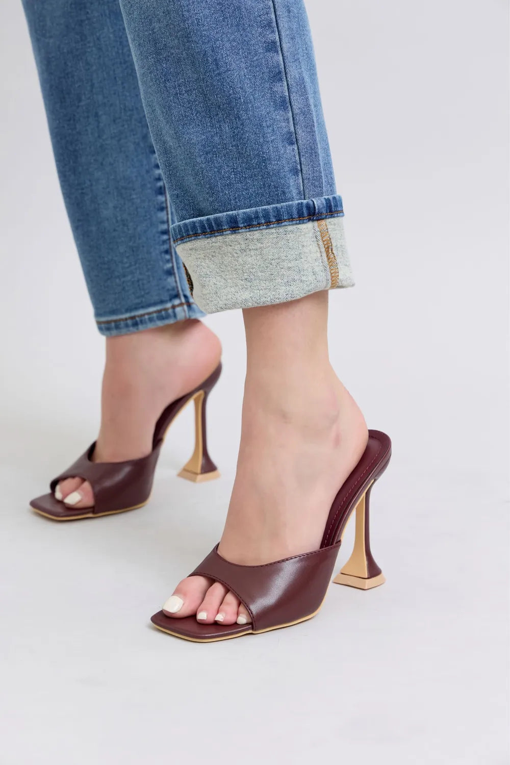 Brown high-heeled shoes worn with rolled-up jeans on a light background