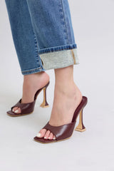 Brown high-heeled shoes worn with rolled-up jeans on a light background