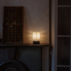 Small lamp on a surface with a textured wall and wooden shelf in the background