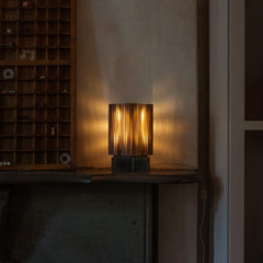 Wooden lamp on a table in a dimly lit room with a vintage shelf in the background.
