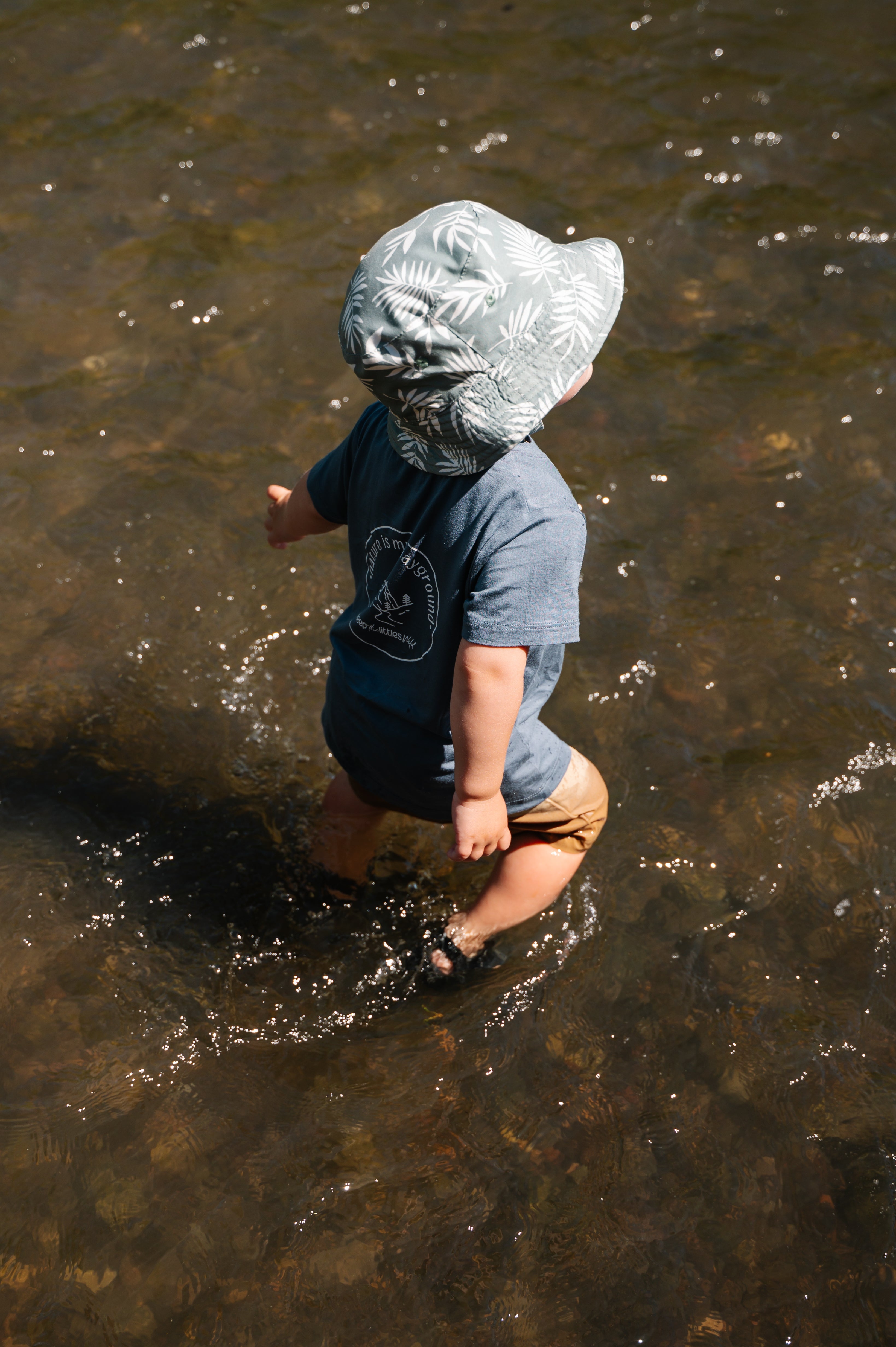 Child wearing a rain hat walking in shallow water