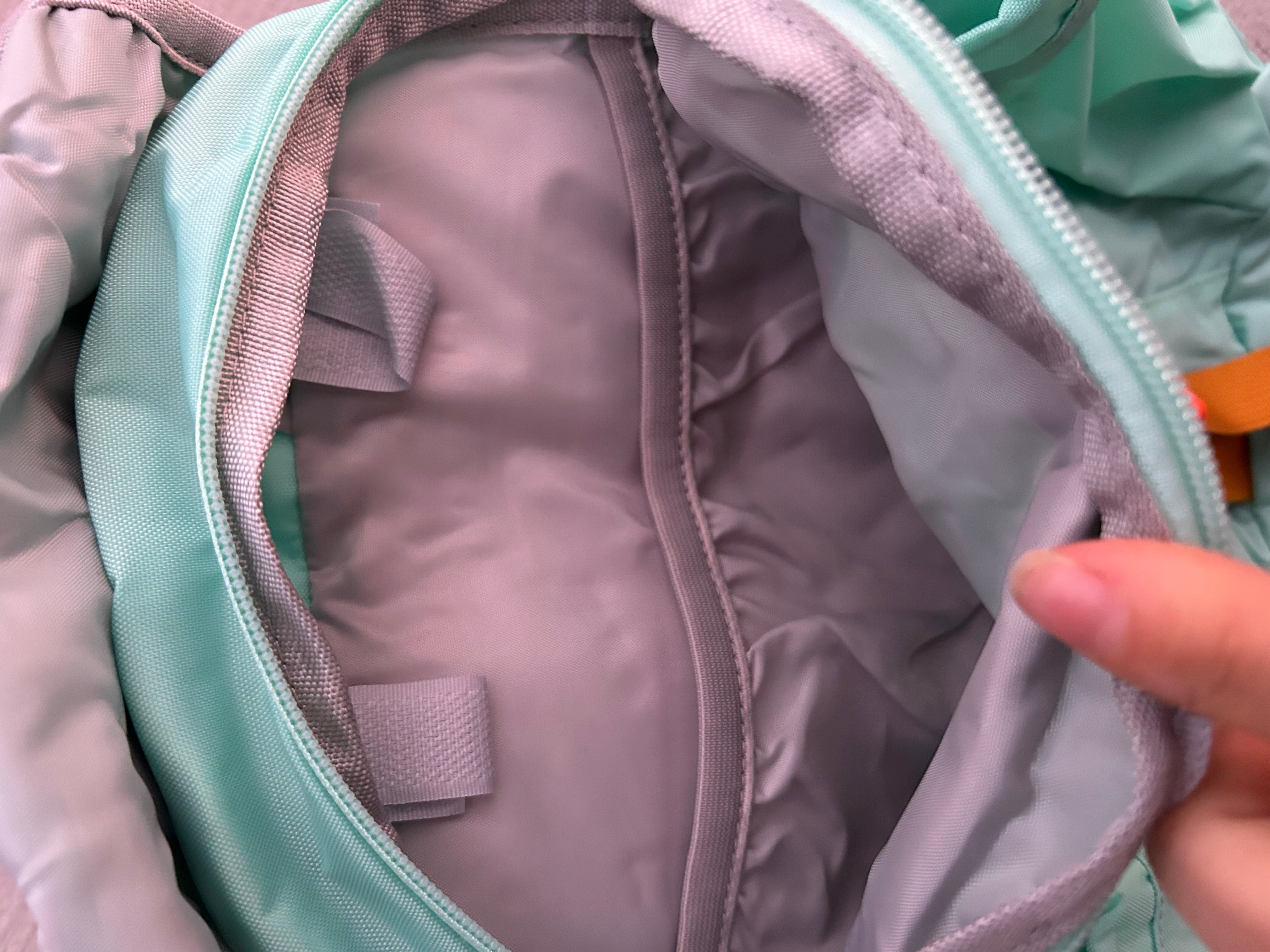 Close-up of a person opening a green and pink bag with a zipper.