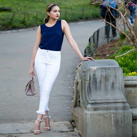 Woman in navy top and white pants standing on a path with greenery in the background