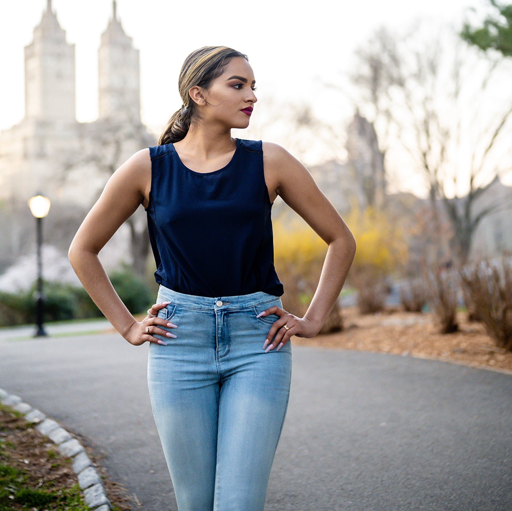 Woman in a navy top and light blue jeans standing outdoors with blurred background
