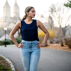 Woman in a navy top and light blue jeans standing outdoors with blurred background