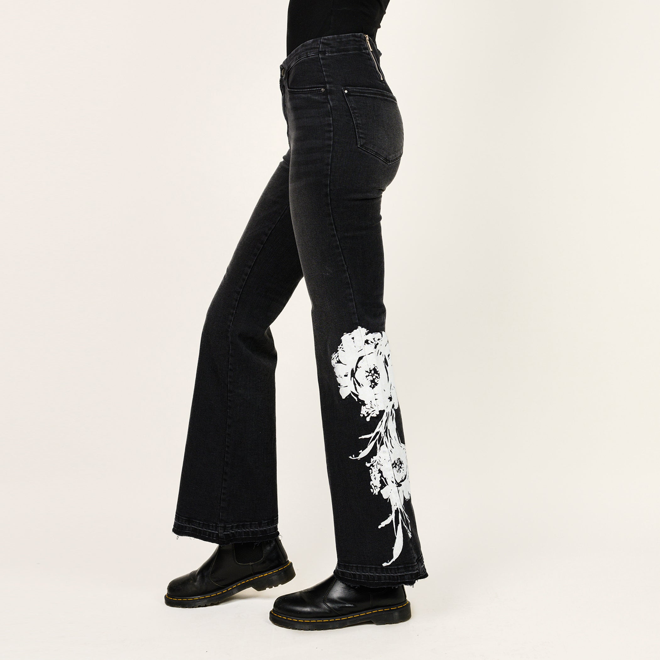Black jeans with white floral embroidery on a beige background