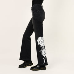 Black jeans with white floral embroidery on a beige background