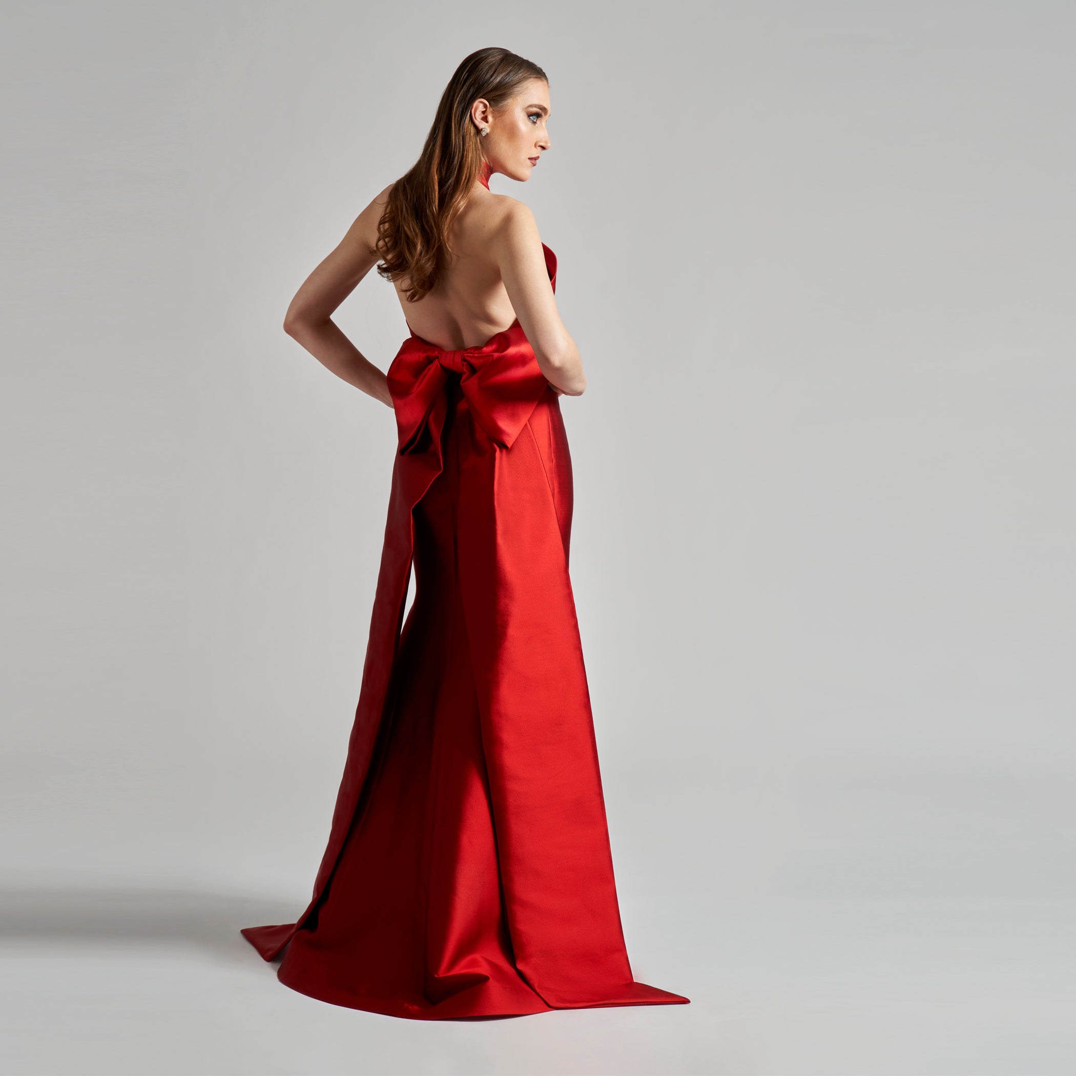 Woman wearing a red evening gown with a large bow on a gray background