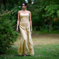 Woman in a gold strapless gown standing in a garden setting