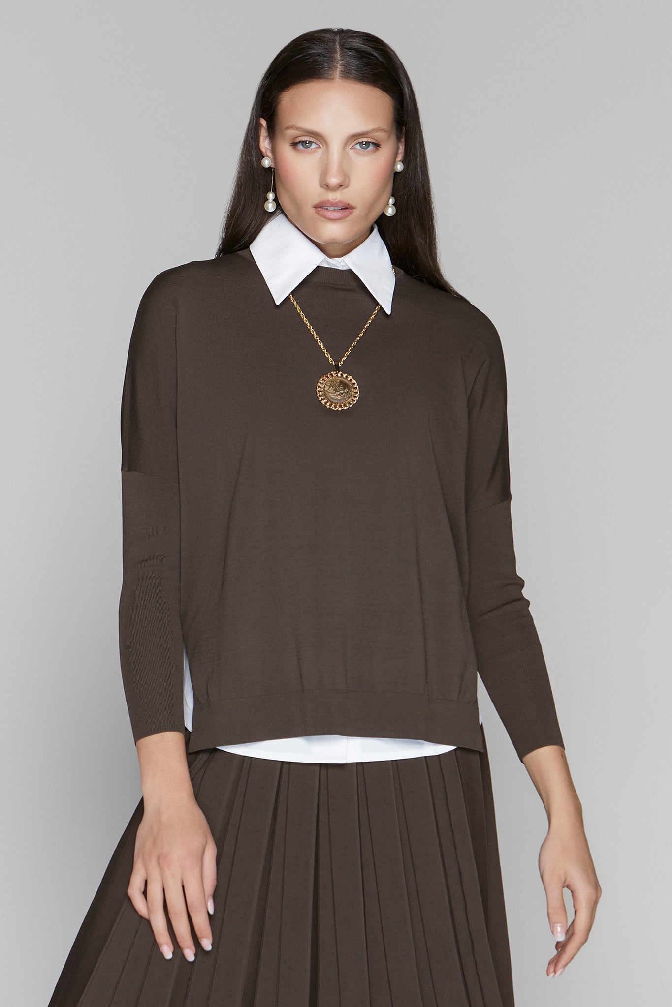 Woman wearing a brown long-sleeve top with a white collar and skirt against a gray background