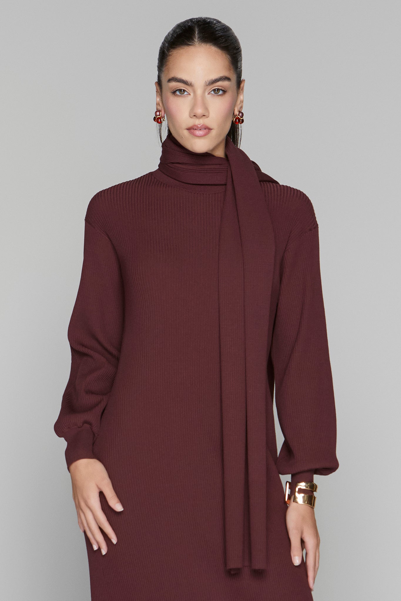 Woman wearing a burgundy dress with a matching scarf against a gray background