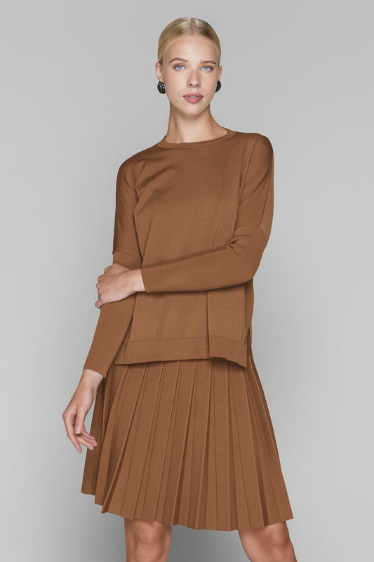 Woman wearing a brown long-sleeve top and pleated skirt on a gray background