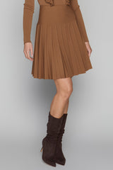 Person wearing a brown pleated skirt and matching knee-high boots on a plain background