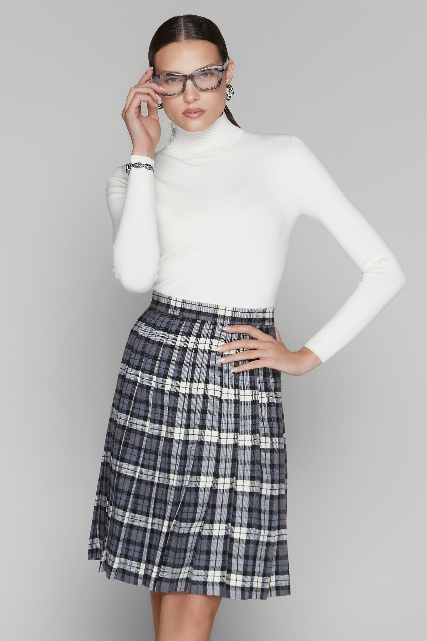 Person wearing a white turtleneck and plaid skirt on a gray background
