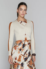 Woman wearing a cream cardigan over a patterned dress on a plain background