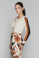 Woman wearing a cream cardigan with brown and black accents and a patterned skirt on a gray background