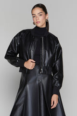 Woman wearing a black textured jacket and skirt on a gray background