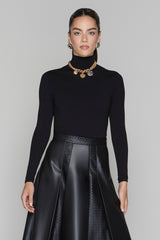 Woman wearing a black turtleneck and black leather skirt with gold jewelry on a gray background