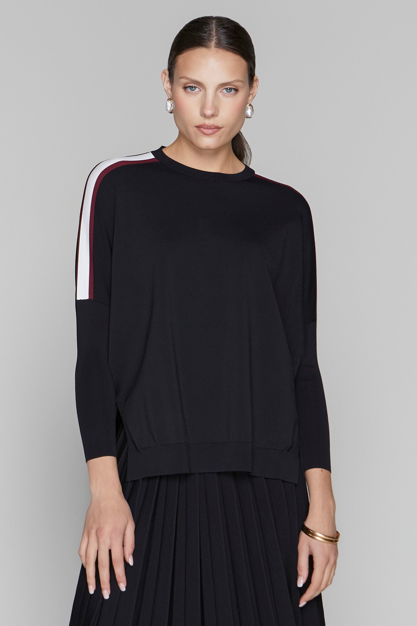 Woman wearing a black sweater with white and red stripes on a gray background